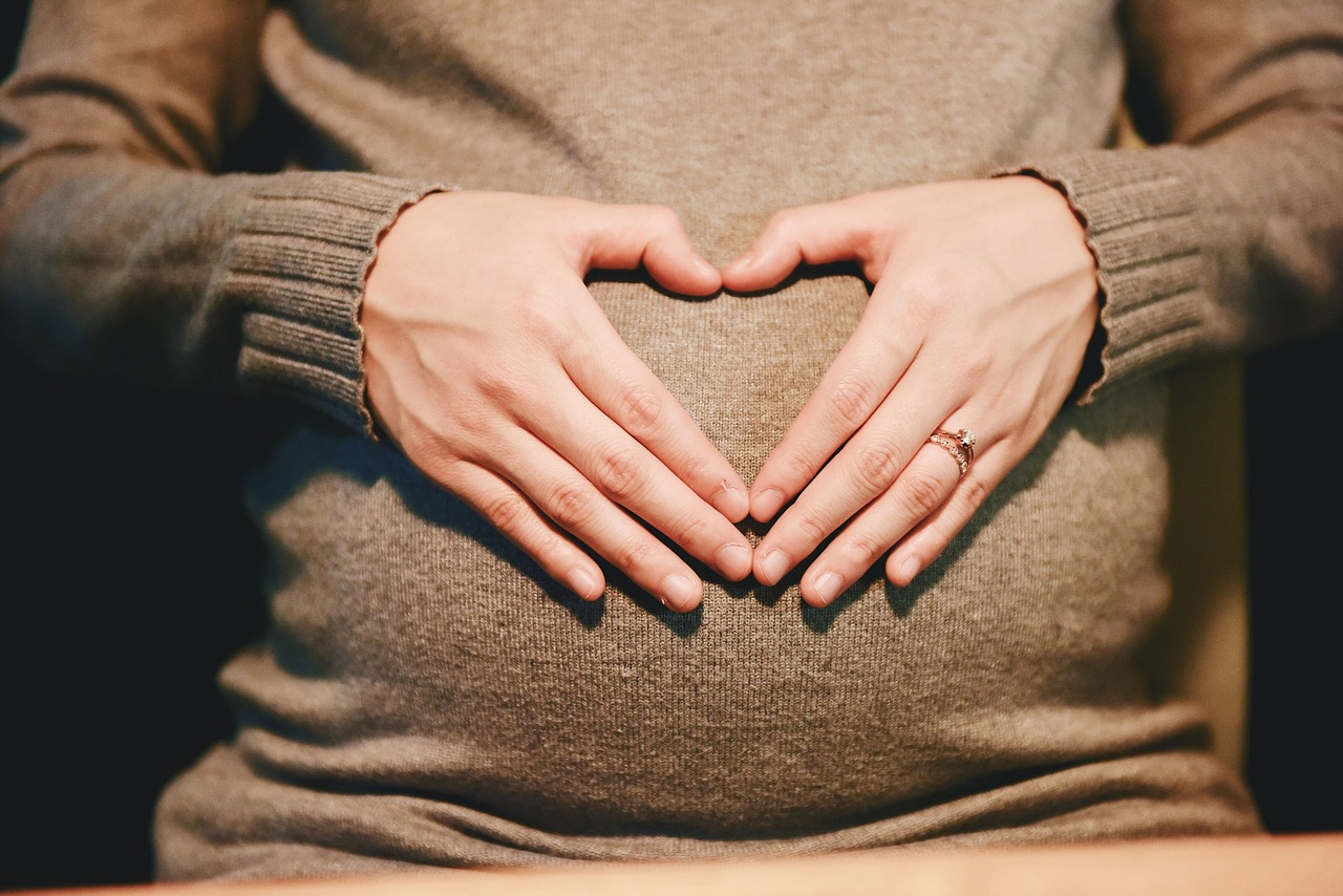A pregnant woman making a heart with her hands on her belly.