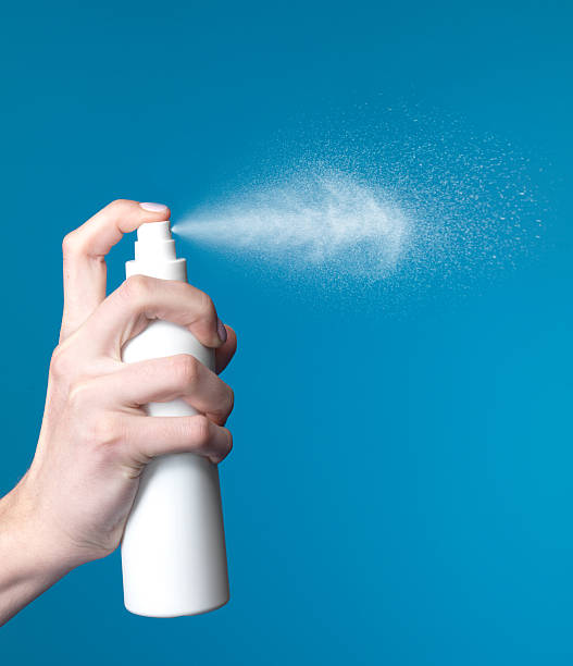 Hand spraying a deodorant spray, releasing a fine mist