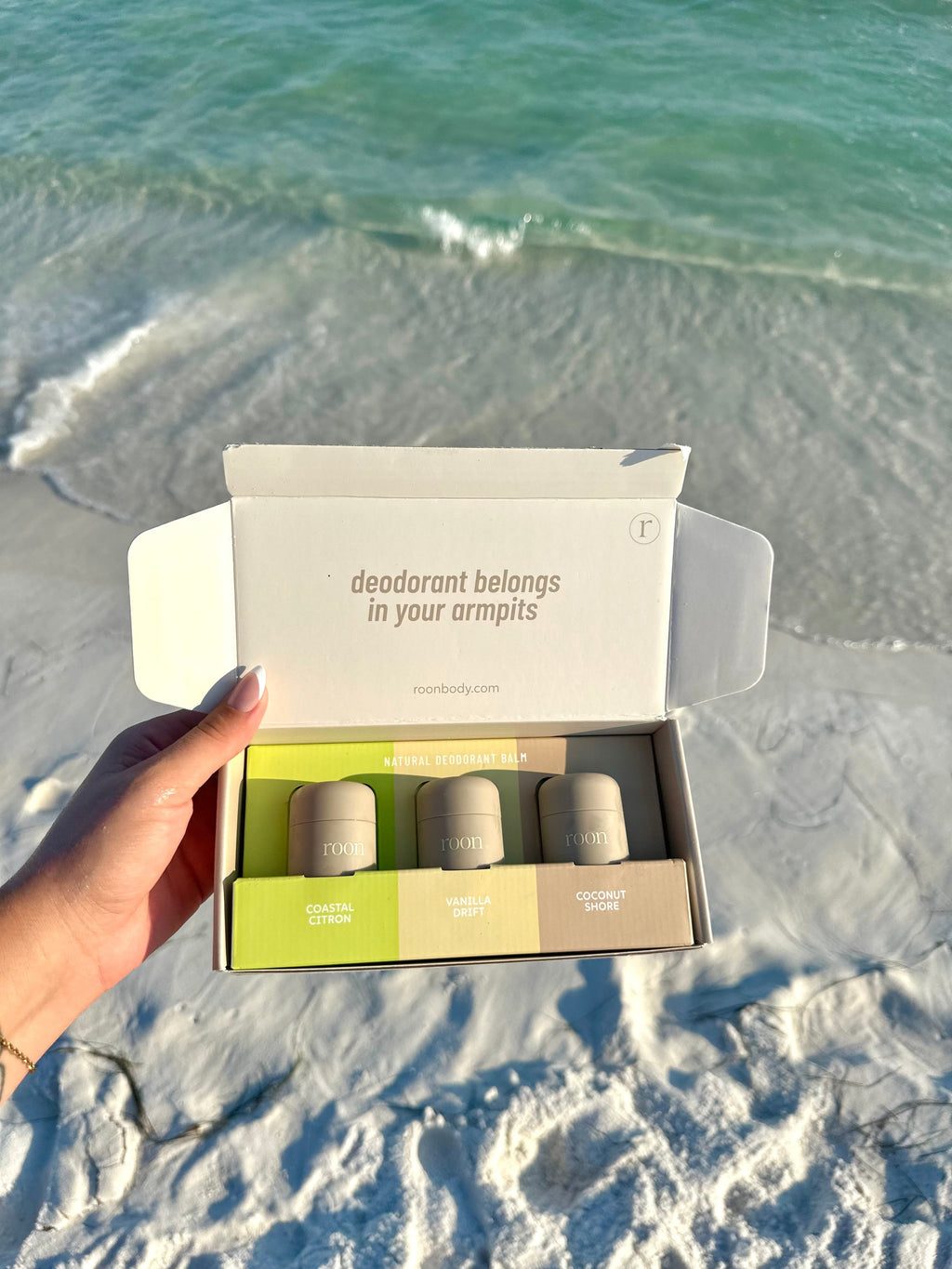 The Roon Discovery Set mailer box opened at the shoreline — three mini deodorant balms: Coastal Citron, Vanilla Drift and Coconut Shore
